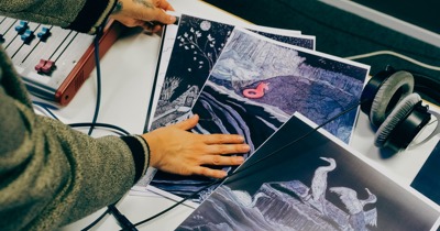 Une main qui touche des illustrations, une sonsole sonore sur la gauche