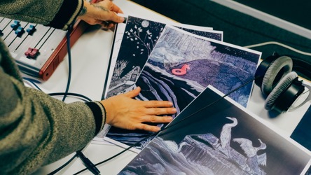 Une main qui touche des illustrations, une sonsole sonore sur la gauche