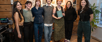 Six personnes se tiennent devant un paneau de documents, l'une d'entre elles tient un livre