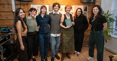 Six personnes se tiennent devant un paneau de documents, l'une d'entre elles tient un livre