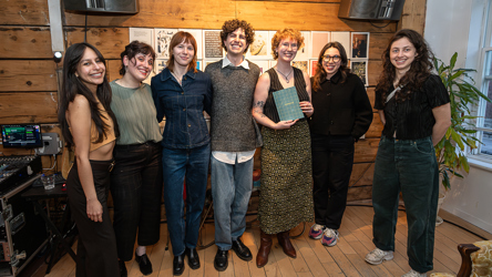 Six personnes se tiennent devant un paneau de documents, l'une d'entre elles tient un livre