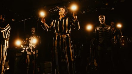 Des individus en costumes noirs et blancs, sur scène, qui tiennent des globes de lumière dans leurs mains