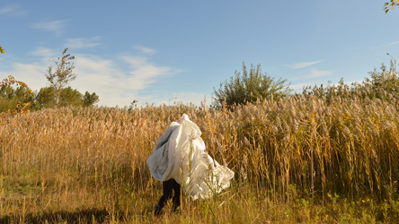 Une personne recouverte d'une bâche, debout, dans un champs de blé