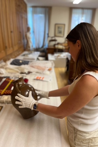 Un femme tient un vase brun avec des gants blancs