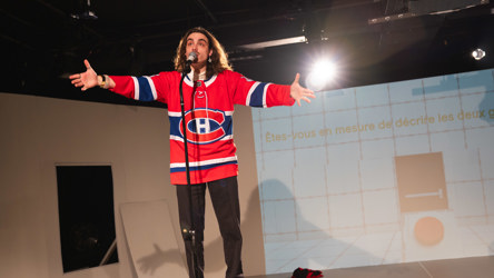 Un homme aux cheveux longs et vêtu d'un gilet de l'équipe de hockey des Canadiens de Montréal parle devant un micro, les bras ouverts