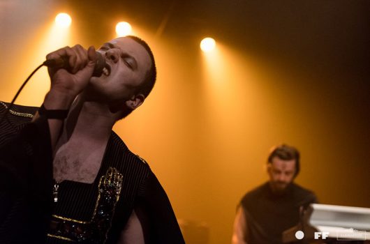 Un homme déguisé chante dans un micro qu'il tient, un musicien en arrière plan