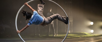 Artiste de cirque en roue cyr, vêtu de bleu et brun