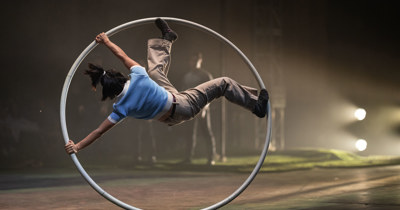 Artiste de cirque en roue cyr, vêtu de bleu et brun
