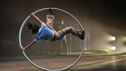 Artiste de cirque en roue cyr, vêtu de bleu et brun