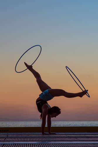 Une acrobate marche sur les mains avec des hula hoops autour des pieds