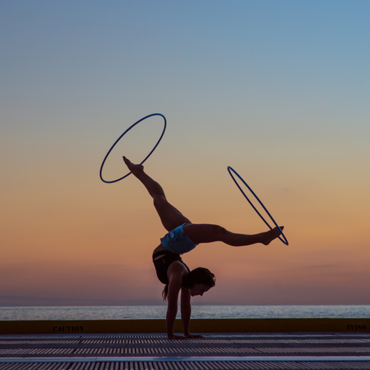 Une acrobate marche sur les mains avec des hula hoops autour des pieds