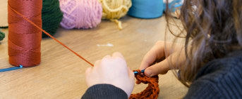 Une personne qui fait du crochet, avec des bobines de laine mutlicolores en fond