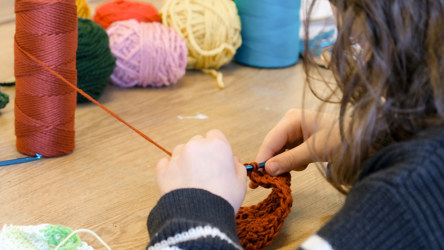 Une personne qui fait du crochet, avec des bobines de laine mutlicolores en fond